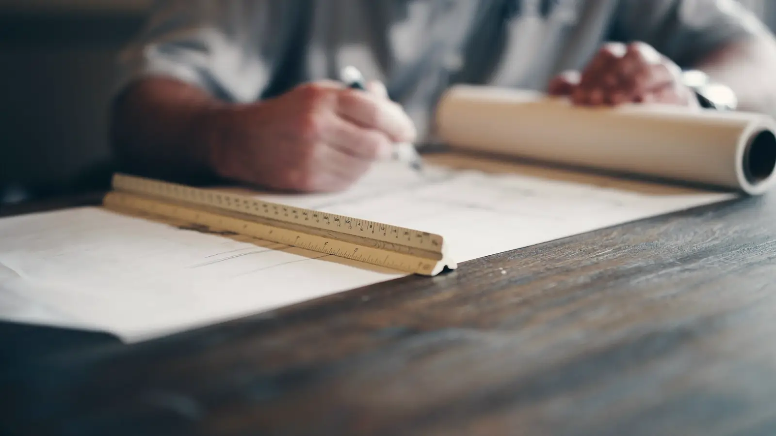Hands marking up a large drawing with a scale rule and a rolled plan