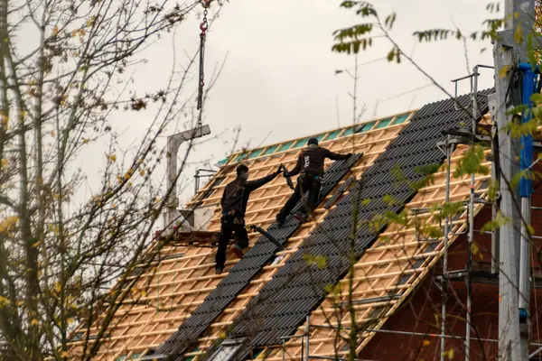 Two roofers laying tiles across battens on a pitched roof