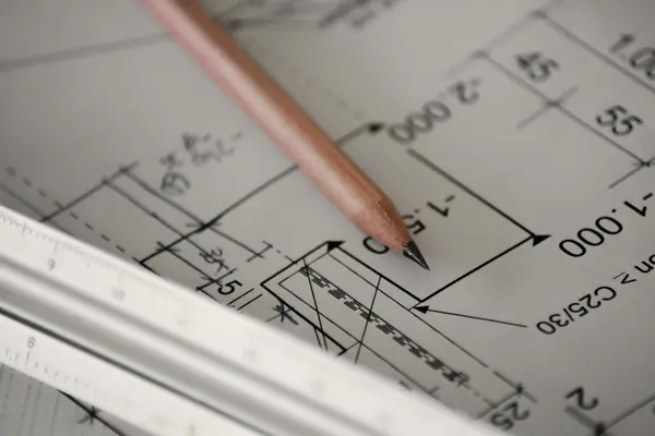 A pencil and scale rule on a dimensioned construction drawing