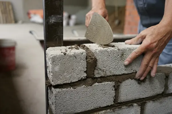 A bricklayer setting a concrete block on a fresh bed of mortar