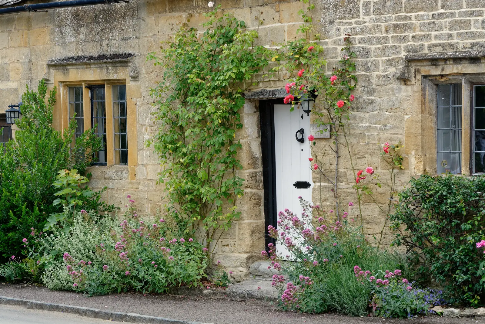 Honey-coloured coursed stone house front with mullioned windows and climbing roses